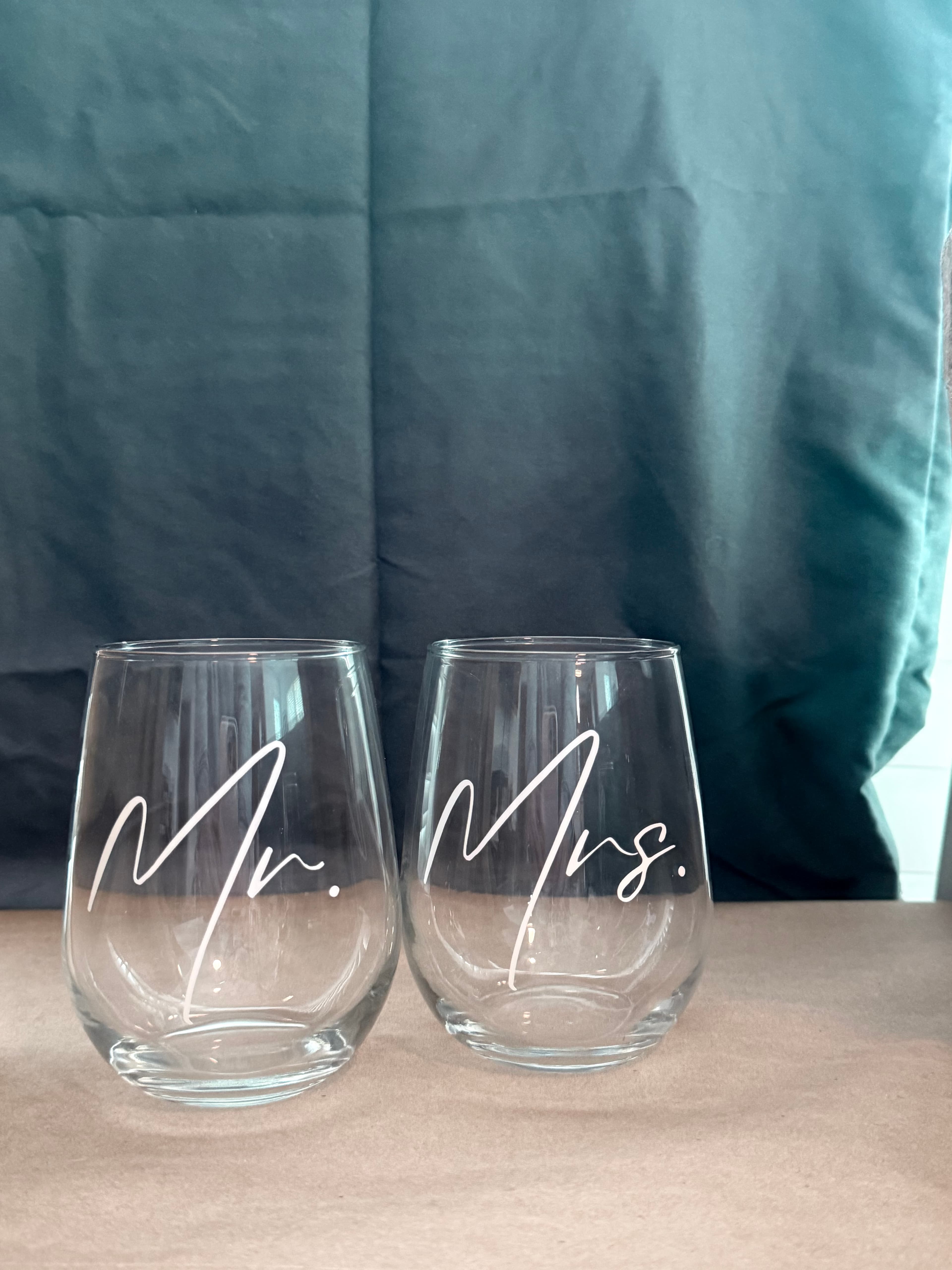 Two stemless wine glasses with white Mr. and Mrs. script against a dark teal background.