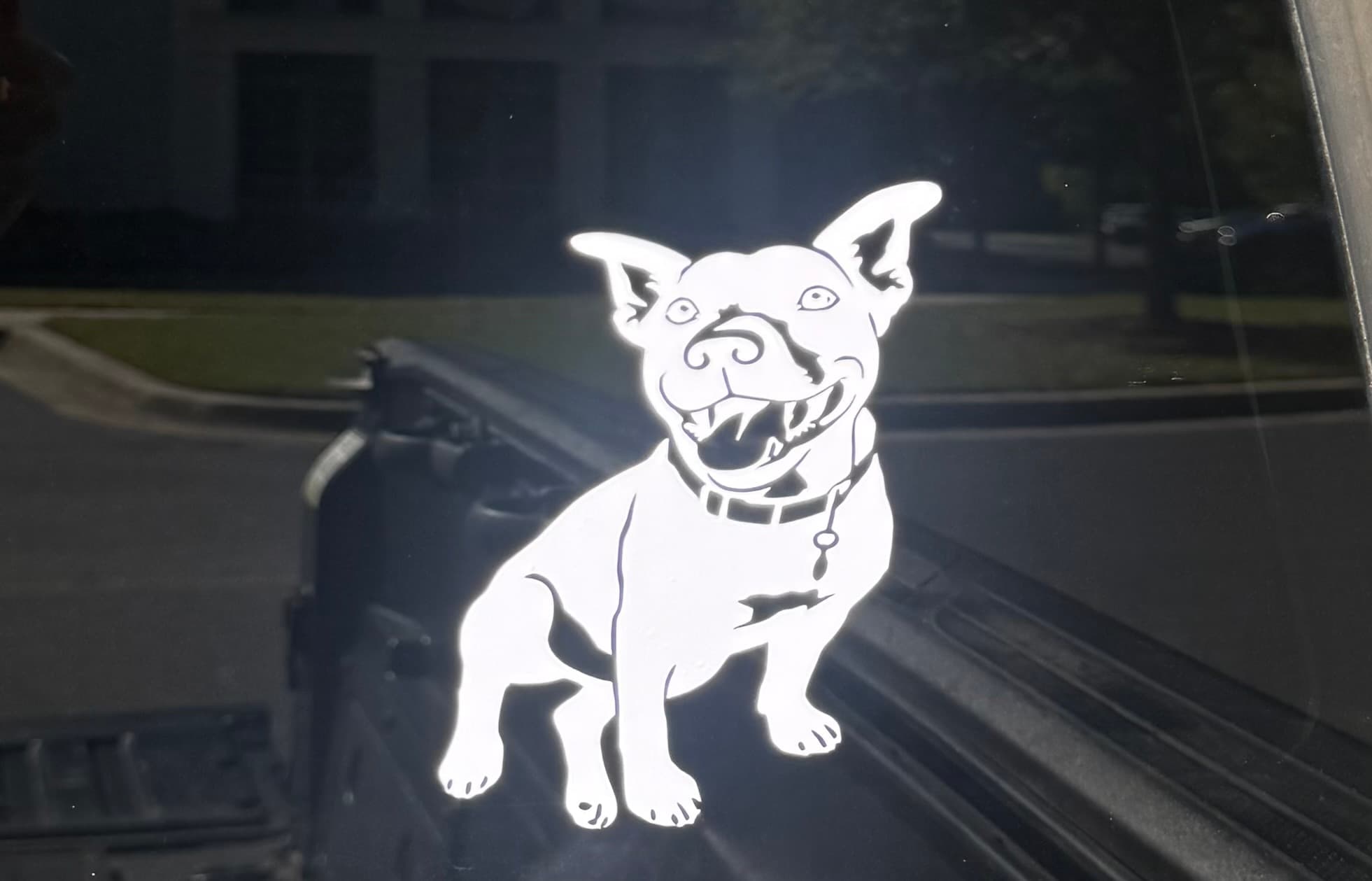 White vinyl decal of a happy, smiling pit bull dog on a dark vehicle window.