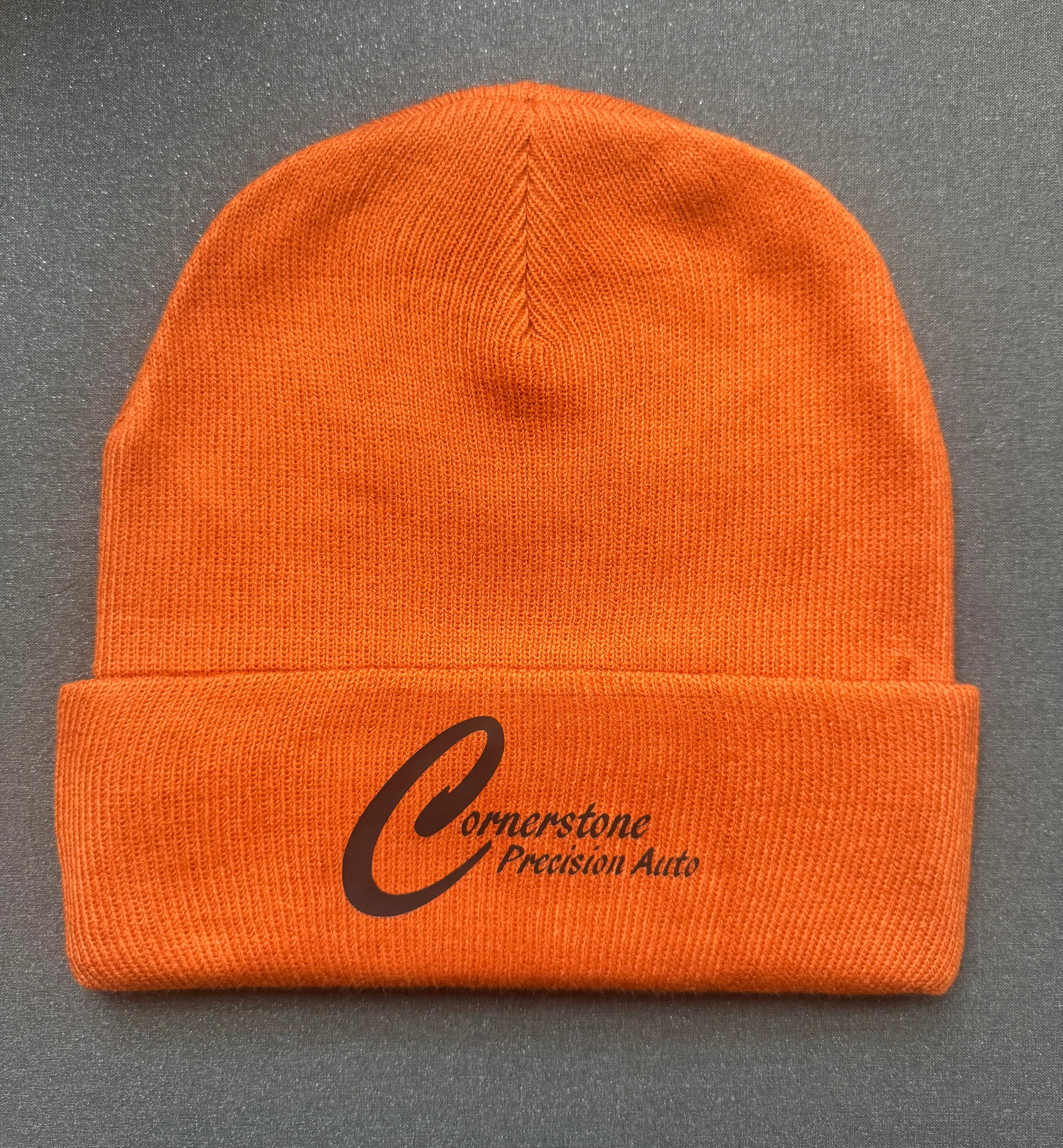 Bright orange knit beanie with a dark Cornerstone Precision Auto logo on the folded cuff.