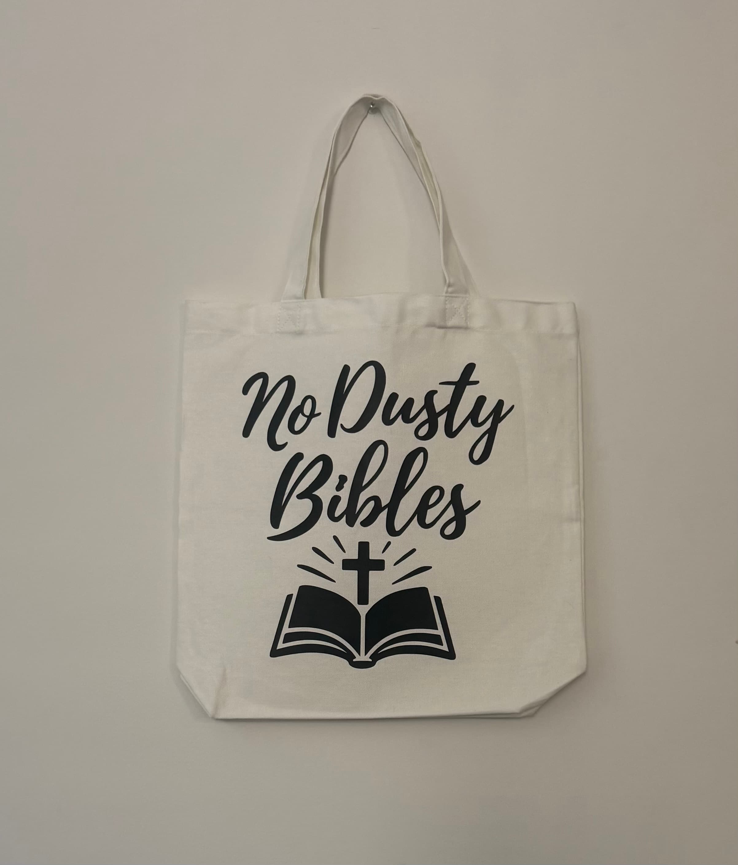 White tote bag featuring black script "No Dusty Bibles" and an open Bible graphic.